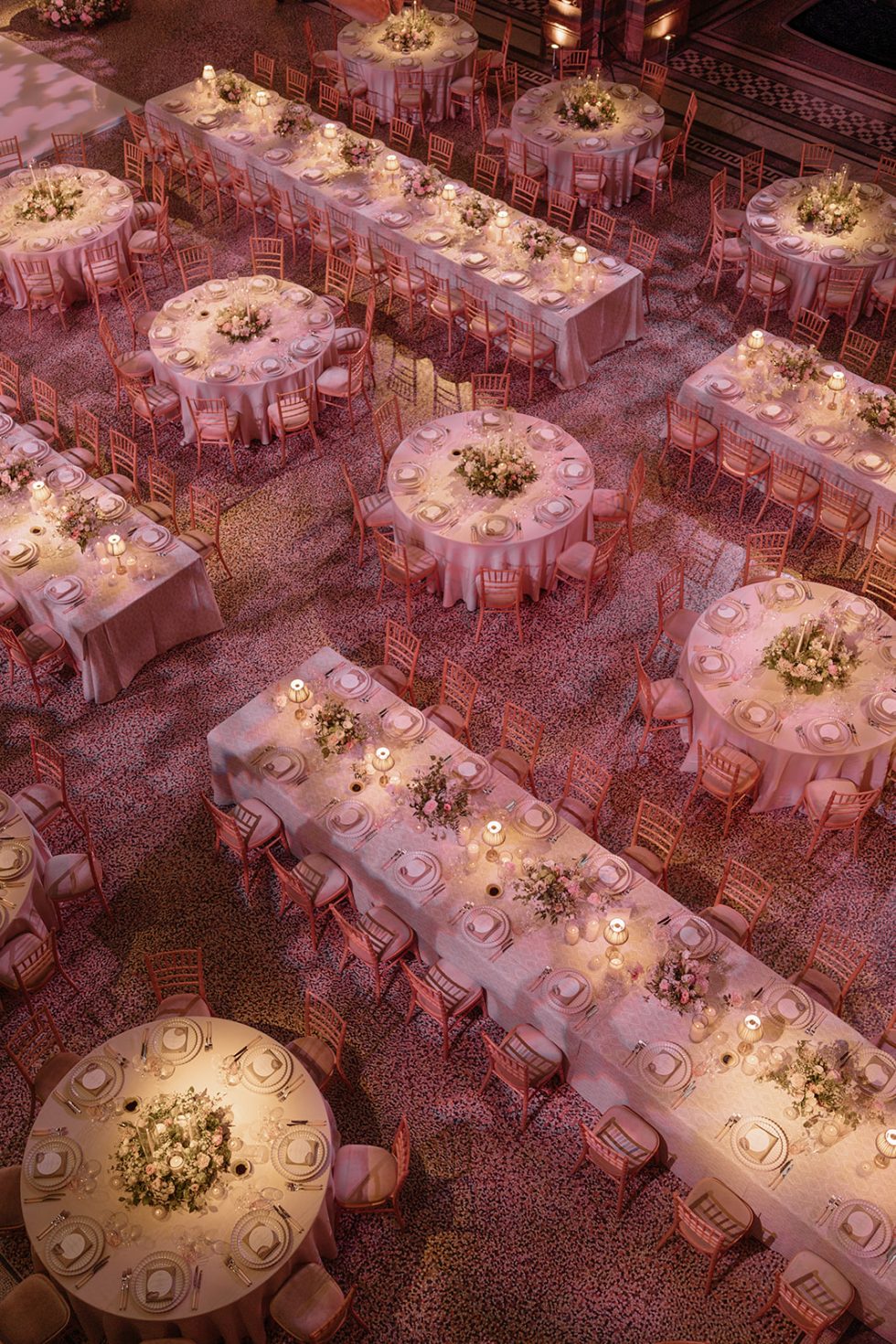 Luxury London wedding reception setup in Hintze Hall at the Natural History Museum, London, featuring long banquet tables and round guest tables dressed in soft ivory linens and elegant floral centrepieces with candles. Designed for a high-end wedding aesthetic with warm romantic lighting and refined tablescapes.